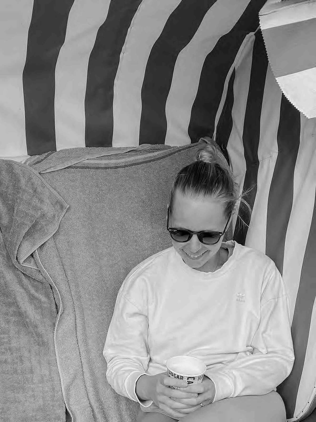 Ich sitze in einem Strandkorb mit Kaffee in der Hand und Sonnenbrille im Gesicht.