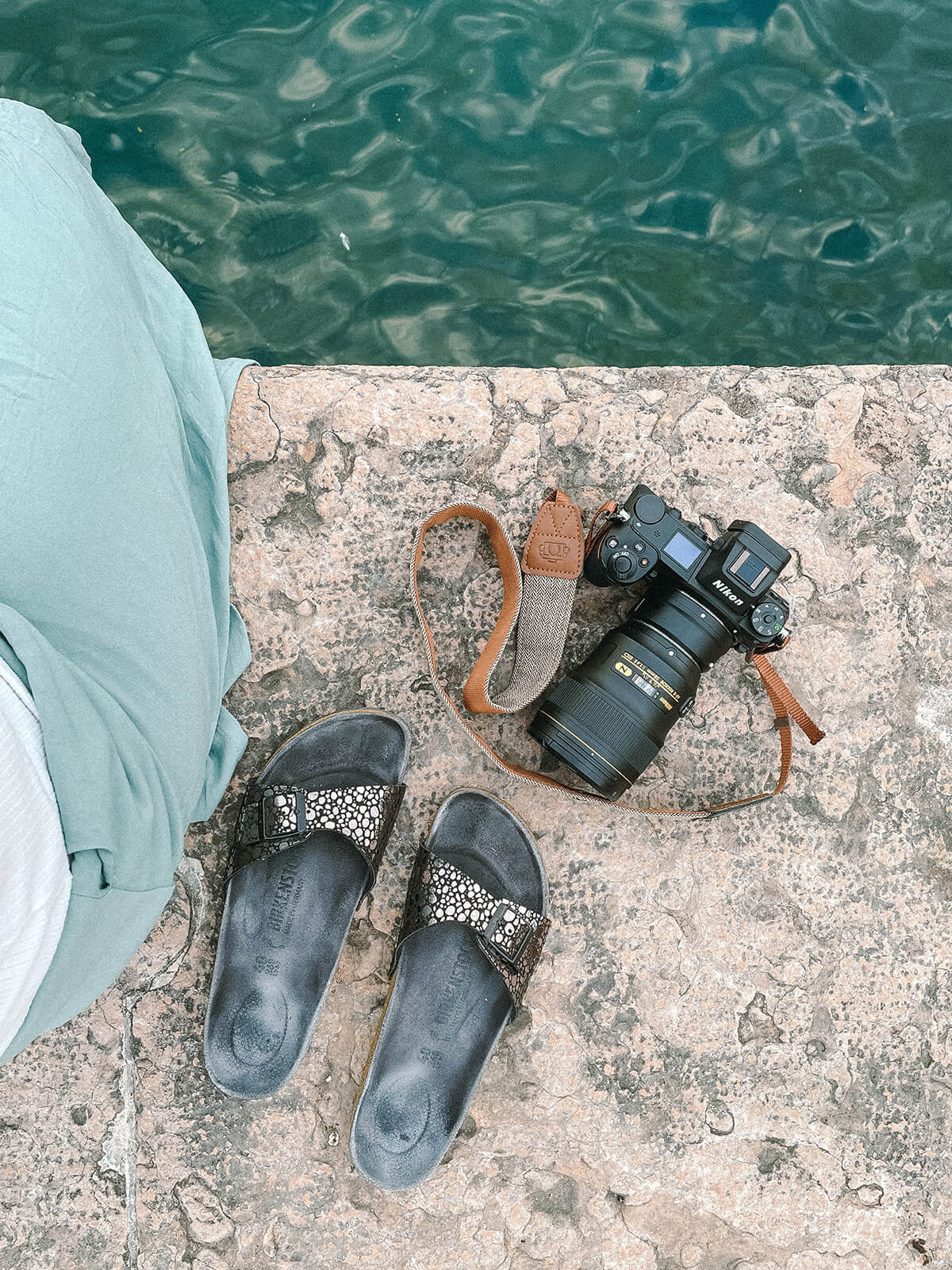 Nikon Kamera auf einer Mauer am Gardasee. Daneben liegen schwarze Birkenstock Sandalen.