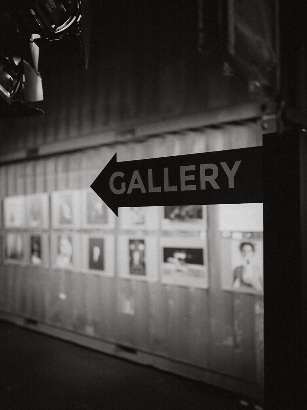 Galleryschild in einer Fotoausstellung. Im Hintergrund sieht man einige Exponate.